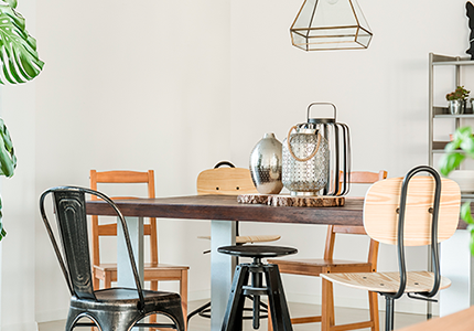 Um espaço com mesa e algumas cadeiras de ferro e madeira com folhagens verdes e itens de decoração.